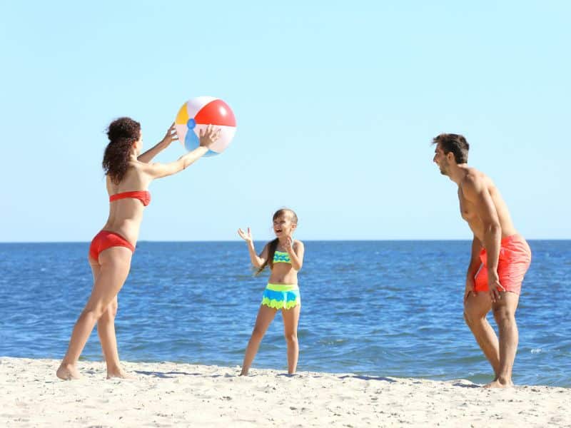 Fröhliche Eltern mit kleinem Mädchen am Wasserball spielen am Strand in Holland
