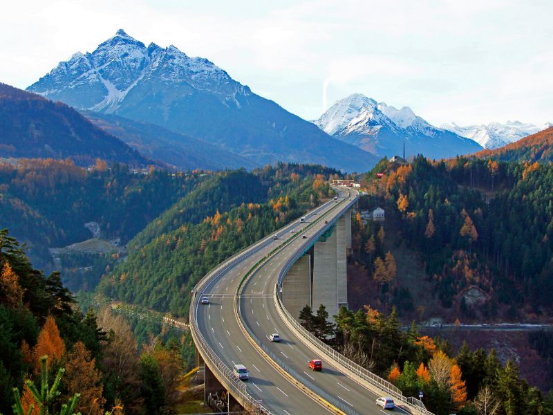 Zweispurige Brenner-Autobahn mit schneebedeckten Gipfeln im Hintergrund.
