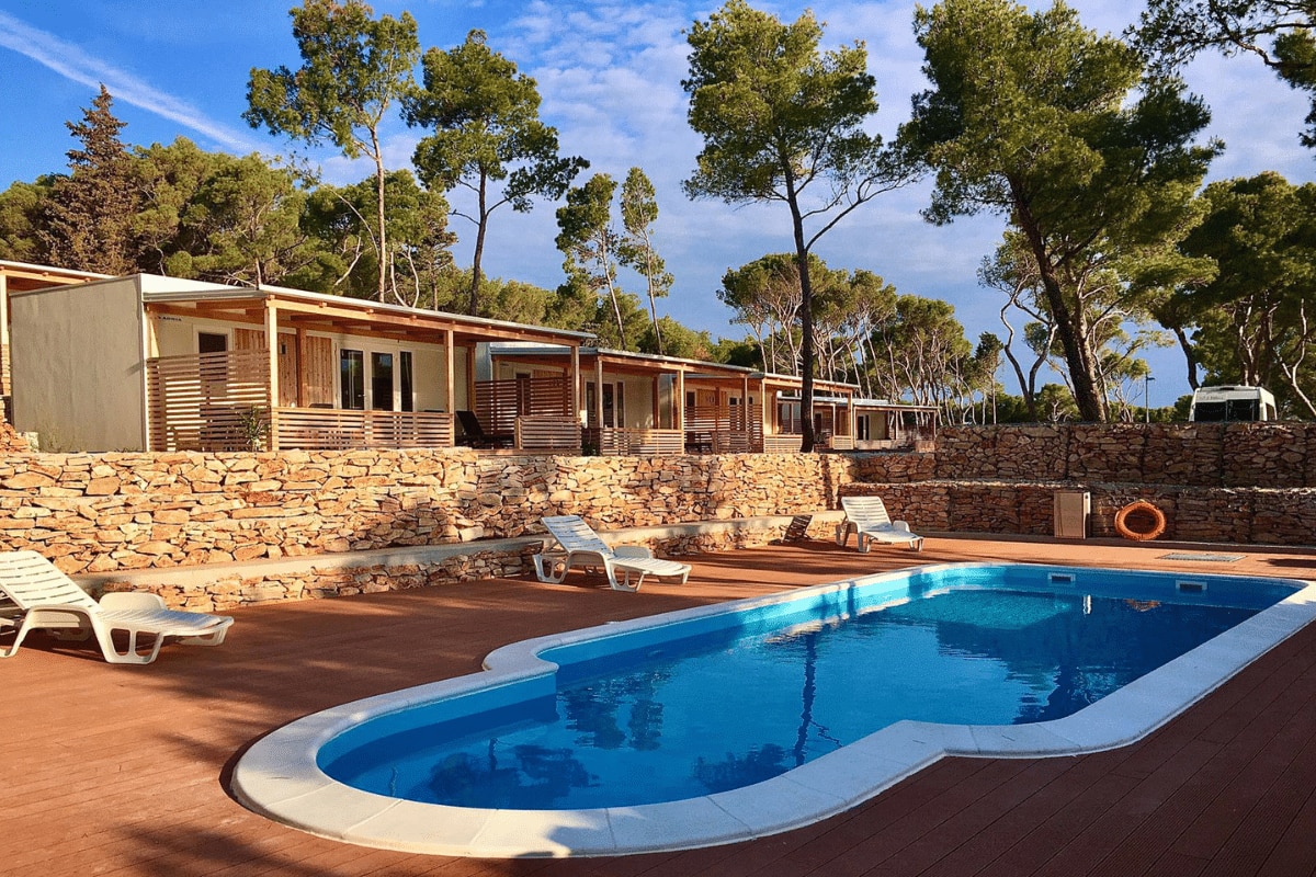 Boutique Campingplatz Bunja – Supetar, Kroatien (Insel Brač) Ferienanlage mit gemütlichem kleinen Pool, Sonnenliegen und Pinienbäumen, die Schattenspenden.