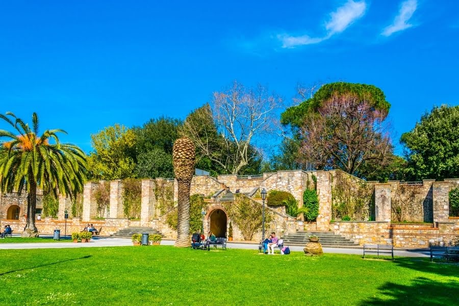 alte bewachsene Stadtmauer mit Palmen und Sitzbänken im Grünen